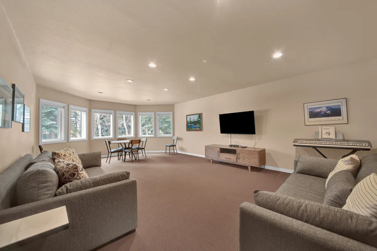This image showcases a spacious living area with multiple sofas arranged for gatherings, a dining table for shared meals, a TV for entertainment, and a piano keyboard tucked beside the seating area. The space is decorated with artwork and invites casual, multi-generational activities such as music practice, movie nights, and family conversations.