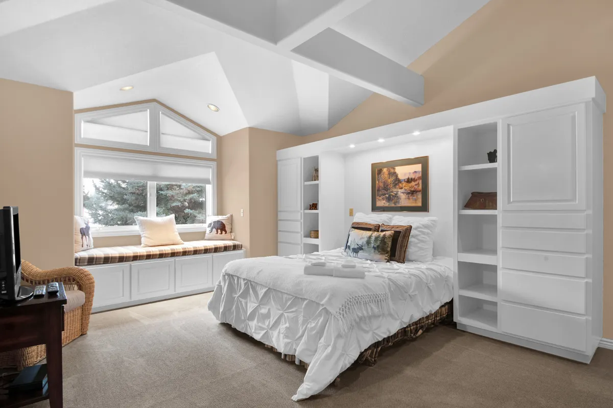 A serene bedroom with a bed dressed in crisp white linens, a cozy window seat perfect for reading, and tasteful artwork on the wall. Soft natural light fills the space, creating a peaceful and inviting retreat.