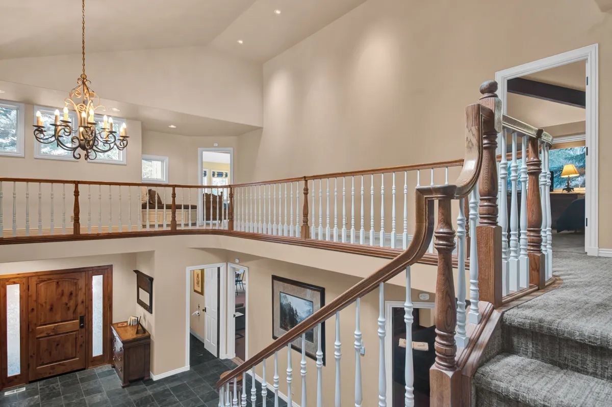 A welcoming view of the home's grand entrance, showcasing a striking chandelier, elegant staircase, and a beautiful front door, all bathed in warm, natural light. The scene captures the feeling of arriving at a luxurious retreat that blends sophistication with comfort.
