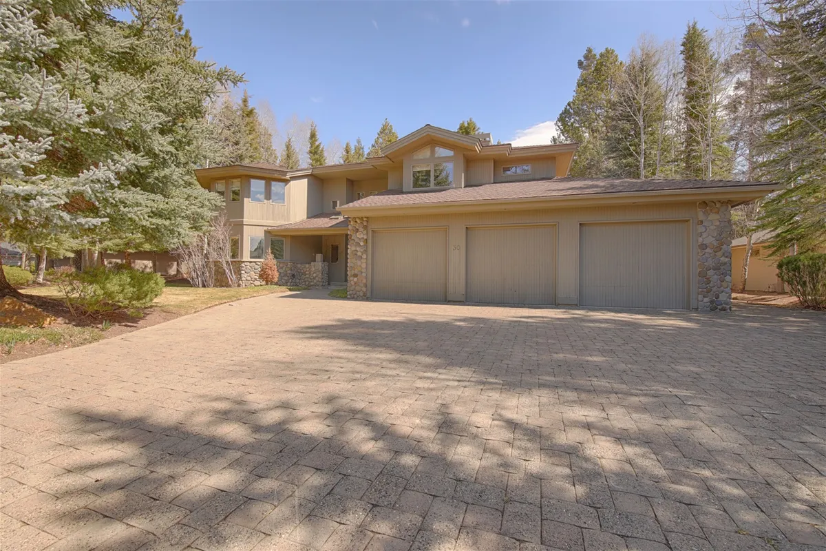 This exterior image highlights the home's large garage, attractive stone facade, landscaped front yard, and the tall trees surrounding the property. The scene evokes a sense of welcoming arrival and shows ample outdoor space where family gatherings and children’s play can take place.