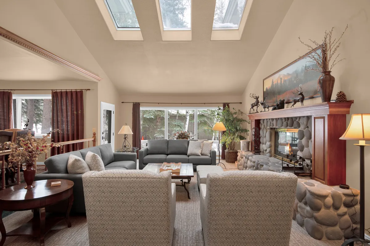 A spacious living space featuring a stylish sofa arrangement, a striking stone fireplace, large windows flooding the room with natural light, and tasteful decorative artwork. The atmosphere is both inviting and upscale, perfectly suited for socializing or quiet family moments.