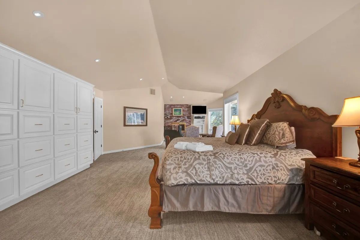 A comfortable bedroom featuring a bed, wardrobe, nightstand, and a cozy fireplace. The room is softly lit, creating a serene setting for relaxation and restful sleep.