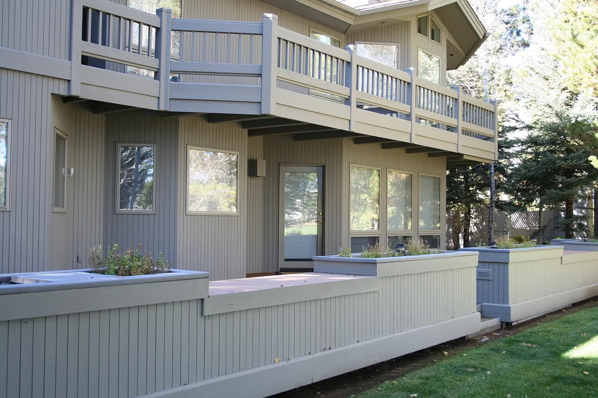 An inviting exterior view featuring a balcony with comfortable seating, expansive windows, and a garden area below. The setting is ideal for relaxing outdoors, enjoying drinks post-game, and taking in panoramic views of the surrounding landscape, likely including the golf course.