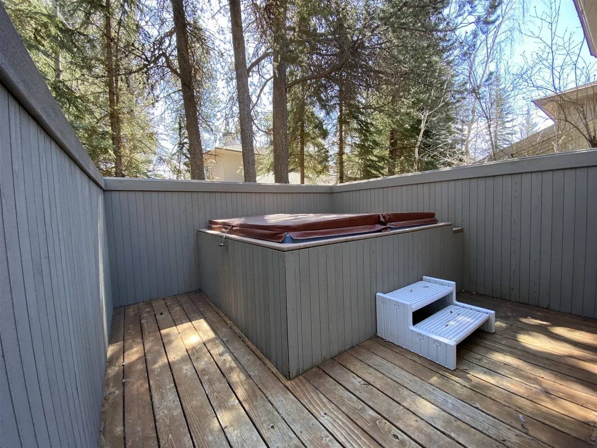 An inviting outdoor hot tub sits on a wooden deck surrounded by trees, offering a tranquil spot to unwind and enjoy the natural surroundings.