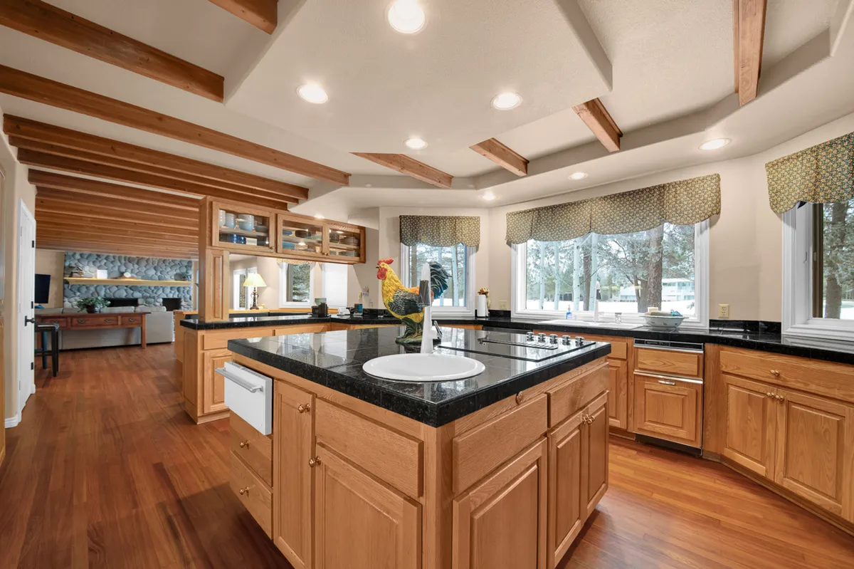 A chef’s kitchen with a central island and black granite countertops, surrounded by rich wooden cabinetry and adorned with charming accents like a decorative rooster. The space is designed for gourmet cooking, socializing, and group meals, embodying the heart of the home.